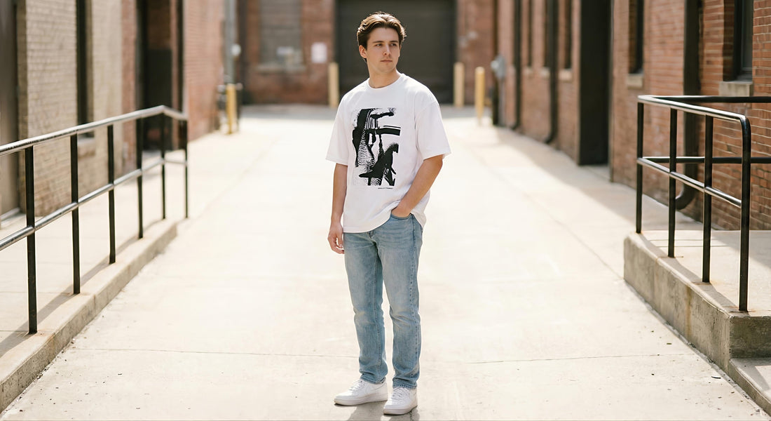 A young man working out in a modern gym with blue ambient lighting. He is wearing an oversized dark grey T-shirt and black shorts, reaching for dumbbells on a rack.