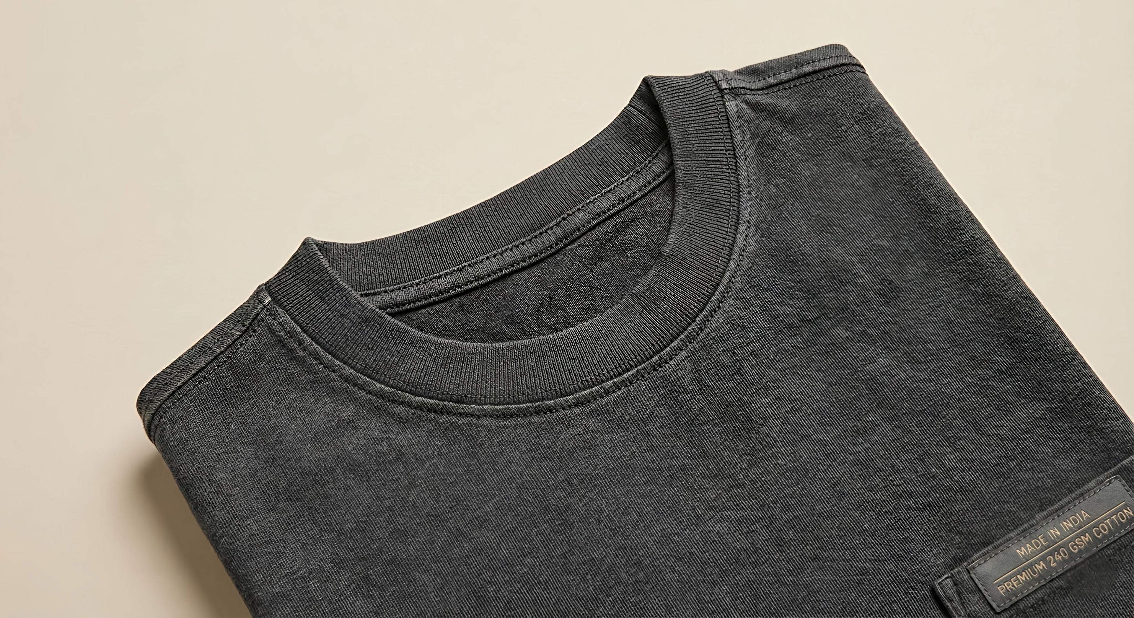 Close-up flatlay detail of a premium black oversized T-shirt showing the thick ribbed neck collar and heavy 240 GSM cotton fabric texture, featuring a 'Made in India' quality label.