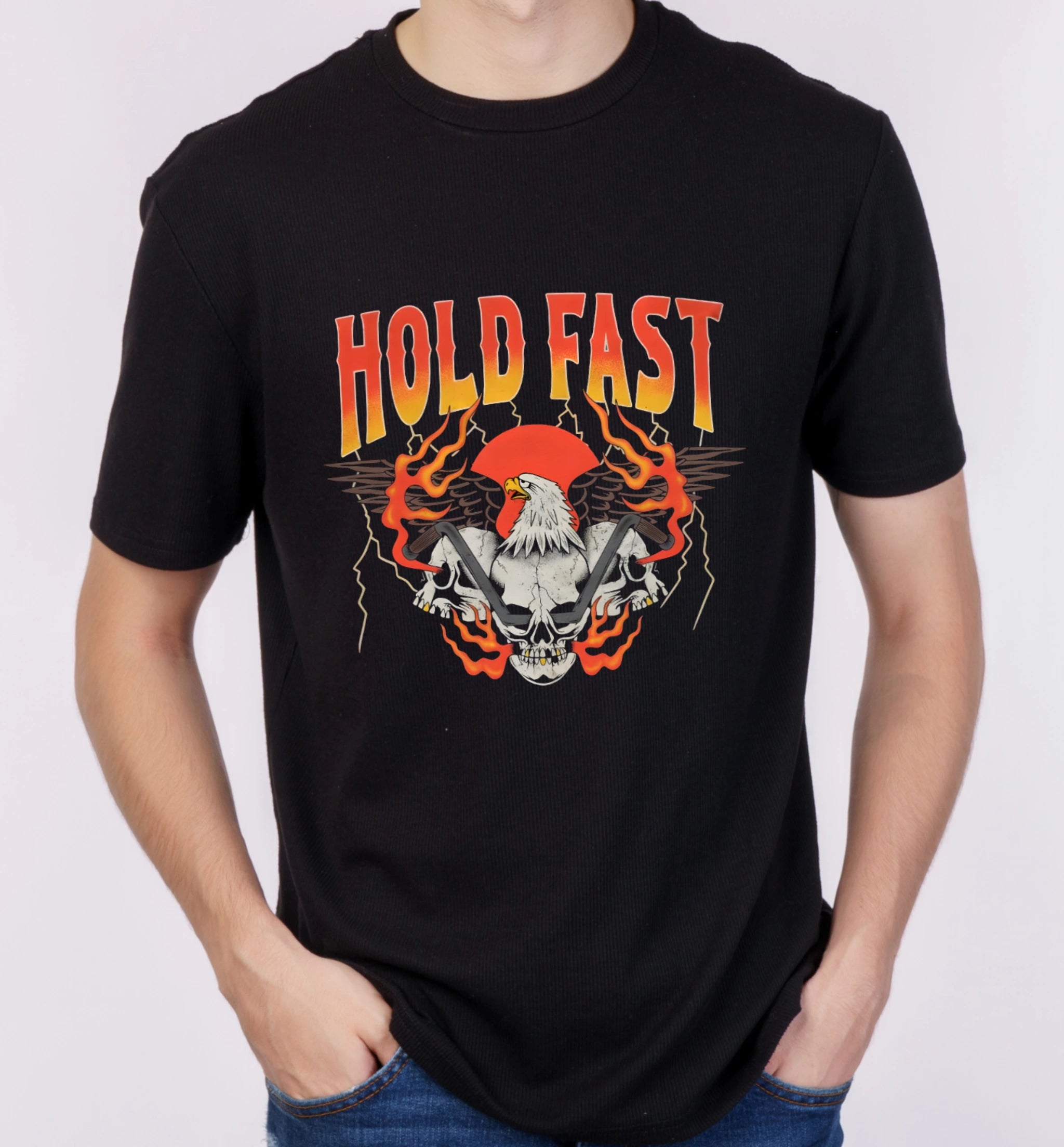 Model wearing AAMS Hold Fast Black Graphic T-Shirt with eagle, skull, flames and slogan design