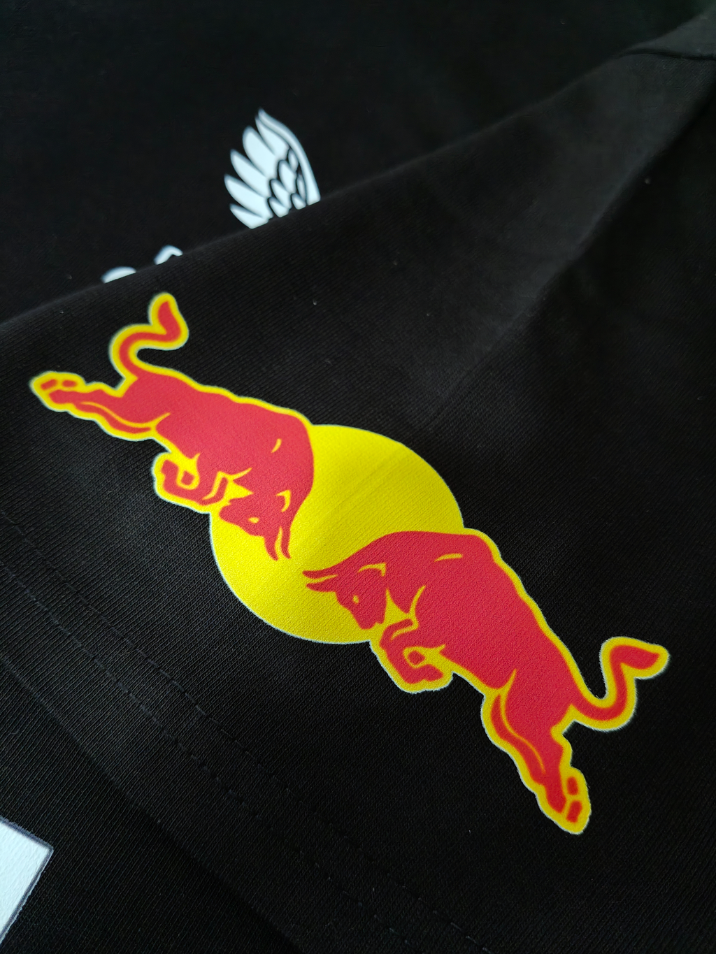 Detail view of the sleeve featuring the classic Red Bull logo with two red fighting bulls against a yellow sun, printed on black fabric.