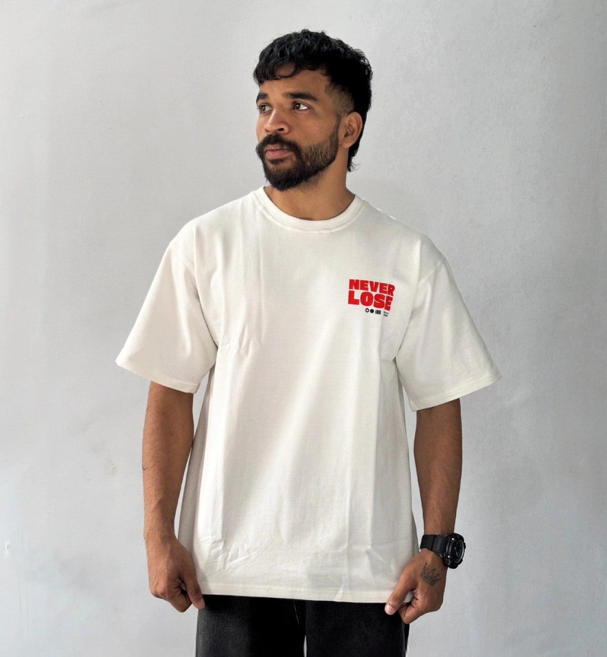 Male model wearing oversized cream Never Lose graphic T-shirt with minimalist red chest print streetwear style