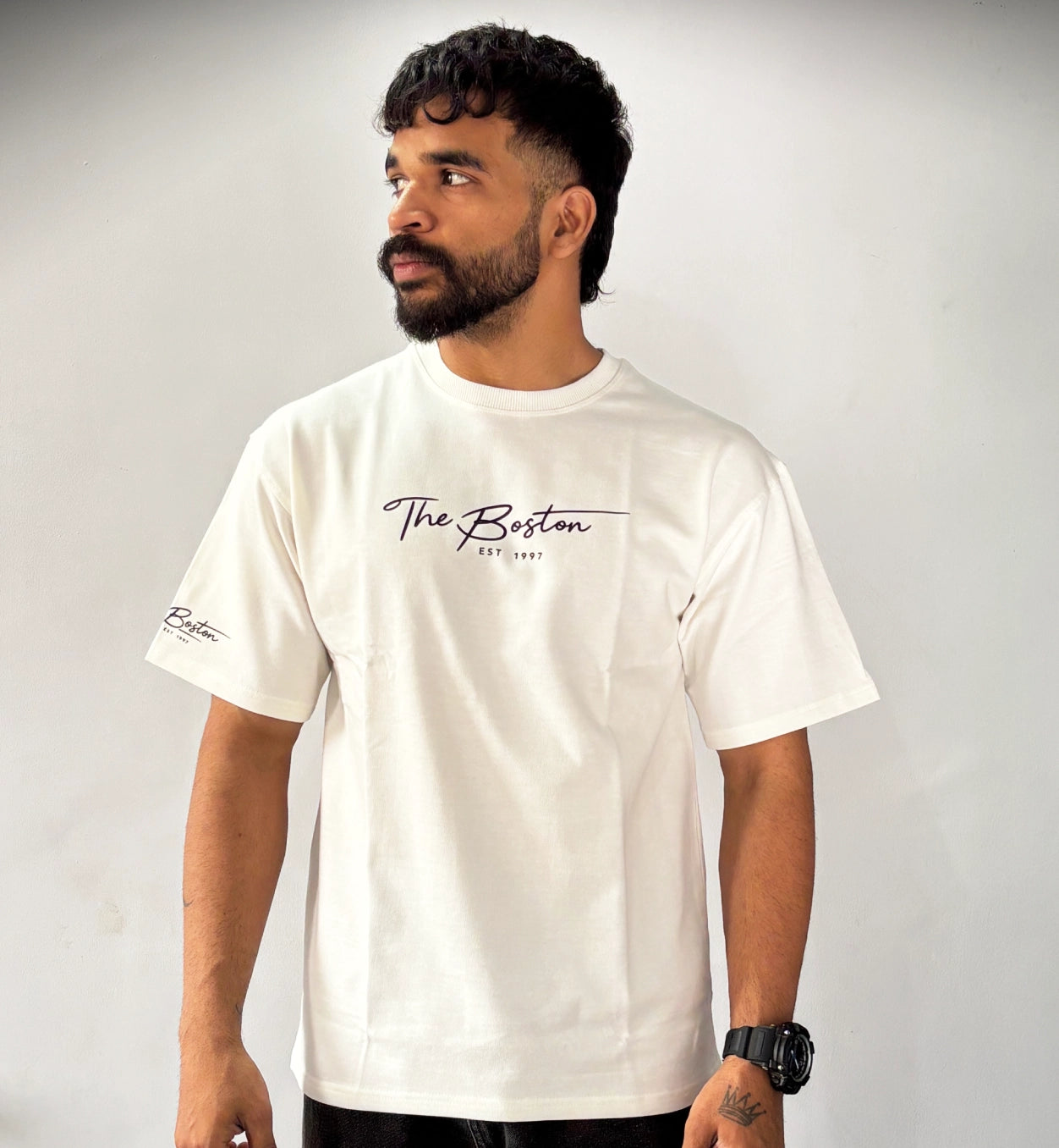 Man wearing cream oversized ‘The Boston EST 1997’ graphic T-shirt by AAMS Wear, minimal premium streetwear tee with script typography design.