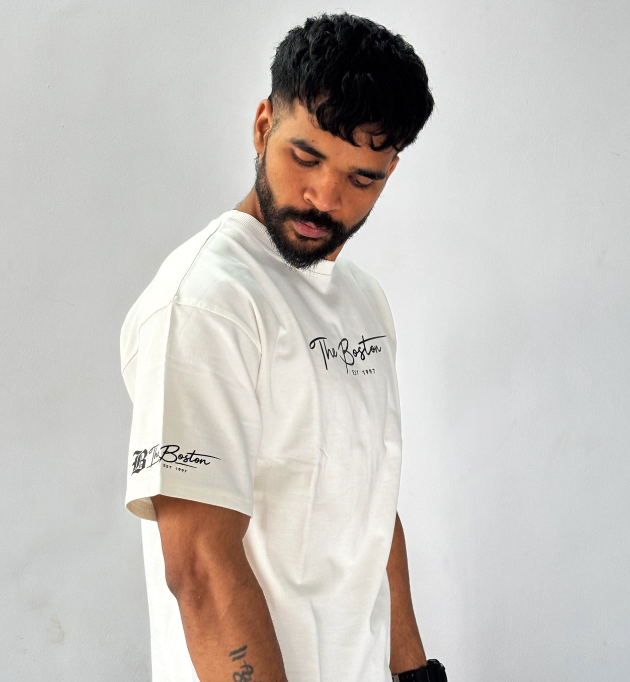 Side view of cream oversized ‘The Boston EST 1997’ printed T-shirt by AAMS Wear showing sleeve branding and relaxed fit.