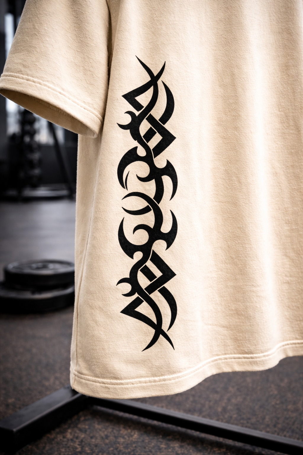 Close-up of off-white oversized t-shirt sleeve featuring bold black tribal vertical graphic print, styled in a gym environment